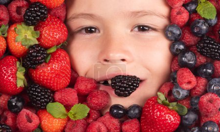 Photo for Berries with kids face close-up. Top view of child face with berri. Berry set near kids face. Cute little boy eats berries. Kid eating vitamins. Close up kids face - Royalty Free Image