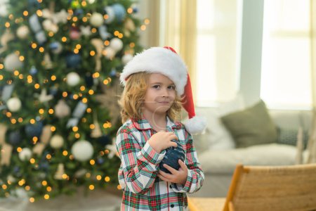 Téléchargez les photos : Joyeux Noël. Enfant fils se prépare à la maison pour la célébration de Noël. Arbre de Noël en arrière-plan. Noël vacances d'hiver concept - en image libre de droit