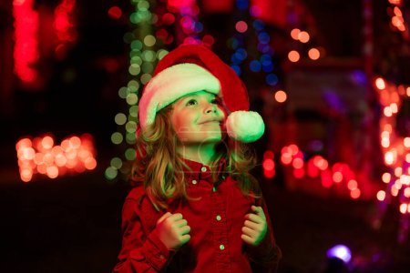 Photo for Happy little kid looks at the sky in the Christmas night. Child in backyard of night house decorated for Christmas Eve celebration - Royalty Free Image