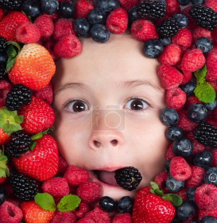 Téléchargez les photos : Alimentation saine pour les enfants. Mélange assorti de fraise, myrtille, framboise, fond de mûre. Les baies se rapprochent du visage des enfants. Des baies fraîches, vue de dessus. Mélange de fruits crus de baies fraîches - en image libre de droit