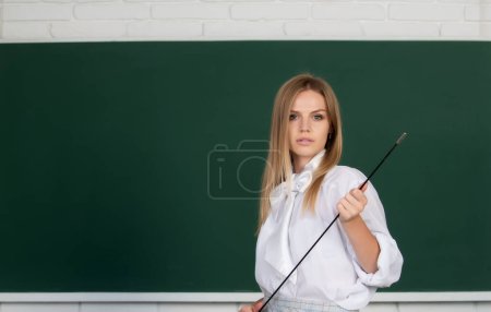 Téléchargez les photos : Professeur sérieux pointant sur la leçon. Jeune femme mignonne avec pointeur enseignant près du tableau noir - en image libre de droit
