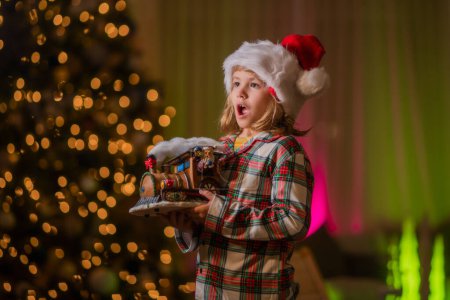 Photo for Kid is having fun near Christmas tree at night home. Child boy 7-8 years old in Christmas pajama enjoying winter holiday evening at home near the night Christmas tree - Royalty Free Image