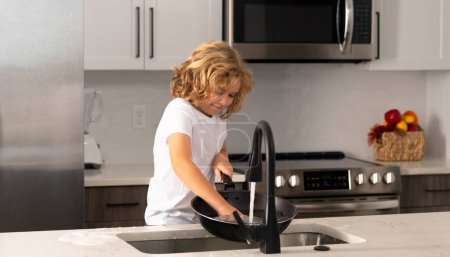 Foto de Los niños ayudan a lavar los platos en la cocina. Limpieza de lavavajillas durante las tareas domésticas - Imagen libre de derechos