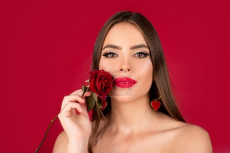 Téléchargez les photos : Beauté femme romantique avec des fleurs roses. Beau maquillage de luxe. Design Saint-Valentin. Portrait de fille mannequin sur fond de studio rouge - en image libre de droit