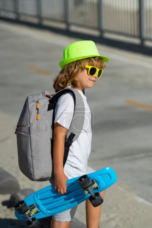 Foto de Feliz niño con estilo en gafas de sol y sombrero de verano de moda posando con monopatín al aire libre. Verano deporte al aire libre y estilo de vida - Imagen libre de derechos