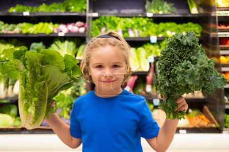 Téléchargez les photos : Enfant avec des légumes à l'épicerie. Alimentation saine pour les enfants. Portrait d'un petit enfant souriant avec sac à provisions à l'épicerie ou au supermarché - en image libre de droit