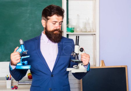 Photo for Portrait of thinking male teacher with microscope, professor, tutor, mentor in school classroom - Royalty Free Image
