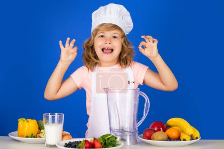Foto de Niño con uniforme de cocina y sombrero de chef preparando verduras en la cocina, retrato de estudio. Concepto de cocina, cocina y comida para niños - Imagen libre de derechos