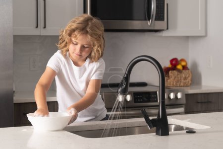 Téléchargez les photos : Enfant avec éponge avec lave-vaisselle liquide fait la vaisselle à la maison cuisine en utilisant éponge de lavage et lave-vaisselle. Nettoyage vaisselle évier éponge lave-vaisselle - en image libre de droit