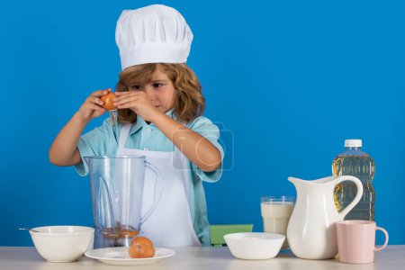 Téléchargez les photos : Chef cuisinier enfant prépare la nourriture dans fond bleu studio isolé. Des enfants cuisinent. Jeune garçon avec tablier et chapeau de chef préparant un repas de légumes sains dans la cuisine - en image libre de droit