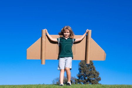 Téléchargez les photos : Rêves de voyage. Enfant volant sur jetpack avec avion jouet sur fond de ciel. Joyeux enfant jouant dans un avion en carton. Le gamin s'amuse dehors - en image libre de droit