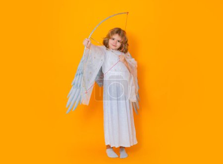 Téléchargez les photos : Cupidon enfant tenir arc et flèche. Petit ange. Portrait d'enfant mignon avec des ailes d'ange isolé sur fond de studio. Petit ange, Saint Valentin. Enfants angéliques - en image libre de droit