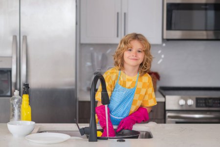 Photo for Portrait of child cleaning in the kithen at home, concept growth, development, family relationships. Child housekeeper washing the dishes on soapy water. Cute Funny boy washing dishes in kitchen - Royalty Free Image