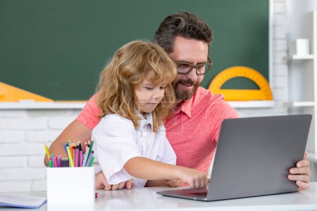 Photo for School teacher and child pupil learning at laptop computer, studying with online education e-learning in class. Teacher helping child student pupil from elementary school in classroom - Royalty Free Image