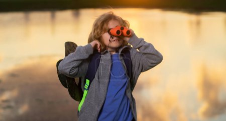 Foto de Childhood. Cute blond kid with binoculars wearing explorer hat and backpack on nature. Child explorer hiking and adventure. Summer vacation, tourism - Imagen libre de derechos