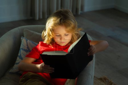 Foto de Portrait of cute blonde child reading interesting kids book story. Child reading book at living room. Kids read books. Little boy sitting on couch in sunny living room watching pictures in story book - Imagen libre de derechos