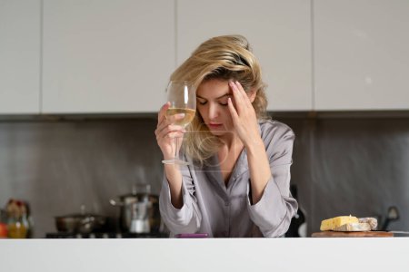 Foto de Upset woman have bad new. Depressed woman in the kitchen in the morning. Sad woman wearing pajama drink wine in home kitchen - Imagen libre de derechos