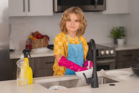 Téléchargez les photos : Dish washing concept. Cute child helping with household, wiping dishes in kitchen. Adorable little helper child housekeeping. Little cute boy sweeping and cleaning dishes at kitchen - en image libre de droit