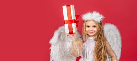 Téléchargez les photos : Angel child banner, isolated studio background. Valentine. Happy smiling cupid girl.Horizontal banner for website header, copy space. Little angel with white wings holds gift - en image libre de droit