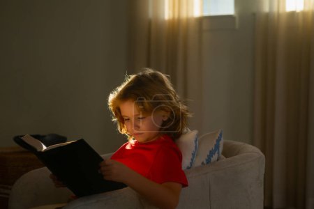 Foto de Schoolboy with book. Kid boy reading book at living room - Imagen libre de derechos