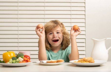 Photo for Kid eating egg. Child in the kitchen at the table eating vegetable and fruits during the dinner lunch. Healthy food, vegetable dish - Royalty Free Image