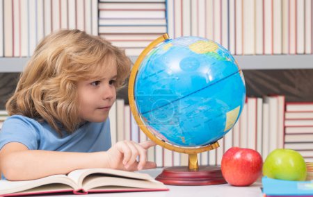 Téléchargez les photos : School pupil looking at globe in library, geography lesson. School and kids. Cute blonde child with a book learning. Knowledge day - en image libre de droit