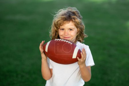 Foto de Outdoor kids sport activities. Cute child having fun and playing american football on green grass park - Imagen libre de derechos