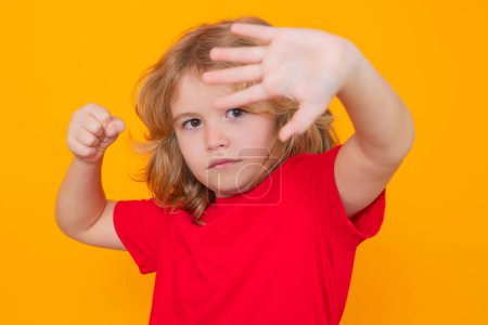 Photo for Kid boy in red t-shirt making stop gesture on isolated studio background. Child with fist gesture fight. Kids protection, bullying, abuse and violence concept - Royalty Free Image
