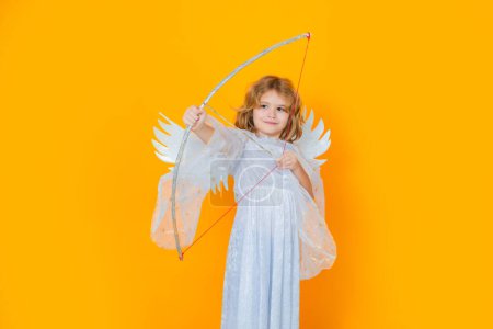 Foto de Angel child shoots a love arrow from a bow on Valentines Day. Cute angel child, studio portrait. Angel kid with angels wings, isolated background - Imagen libre de derechos