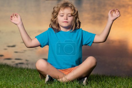 Téléchargez les photos : Child with close eye mindfulness meditating, sit on grass for peace and yoga. Kid relax on summer sunset in park - en image libre de droit