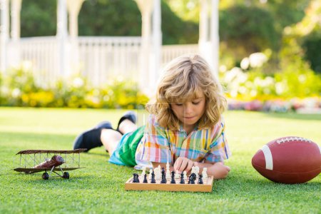 Téléchargez les photos : Chess school outdoor. Child think or plan about chess game, laying on grass in summer park. Intelligent, smart and clever school kids - en image libre de droit