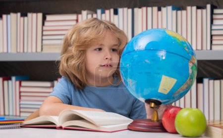 Photo for School pupil looking at globe in library at the elementary school. World globe. Kid boy from elementary school with book. Concept of education and learning - Royalty Free Image