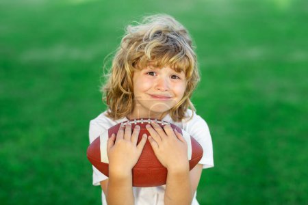 Téléchargez les photos : American style football. Child boy with american football, rugby ball. Cute portrait of a american football player, outdoor - en image libre de droit
