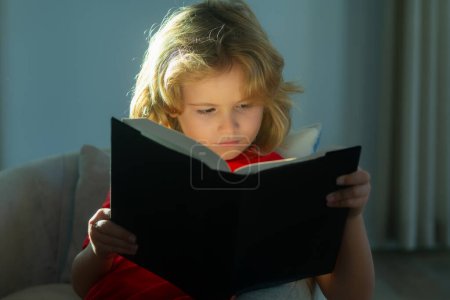 Foto de Elementary school nerd boy pupil read book. Young teenager boy alone at home red book, childhood - Imagen libre de derechos
