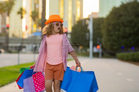 Foto de Amazing excited happy child with shopping packages in hands. Shopper with shopping bag outdoor - Imagen libre de derechos