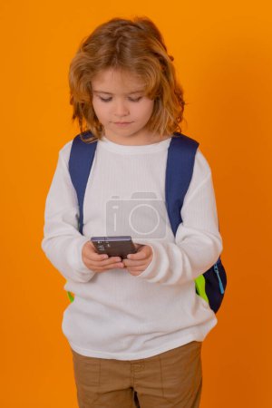 Foto de Isolated portrait of school child. School kid with backpack using phone isolated on yellow studio background - Imagen libre de derechos