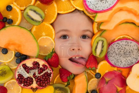 Téléchargez les photos : Kid lick strawberry. Funny child eats organic fruits. Healthy meal nutrition for children. Child eat tasty fruits. Fresh fruit and child face top view. Mix of raw fresh fruits - en image libre de droit
