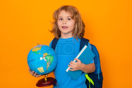 Foto de Smart child, clever school kid. School boy hold world globe and book, isolated on yellow studio background. School and kids. Cute blonde child with a book learning. Knowledge day - Imagen libre de derechos