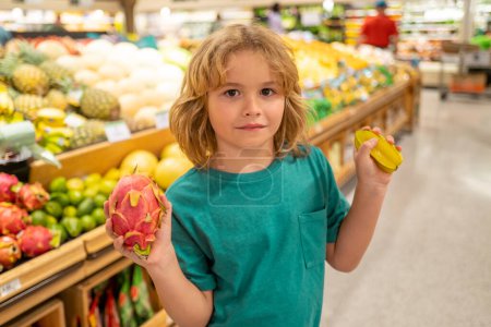 Foto de Kid with fruits. Kid is choosing fresh vegetables and fruits in the store. Child buying food in grocery supermarket. Buying in grocery store. Groceries in the supermarket - Imagen libre de derechos
