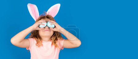 Foto de Easter banner, mockup copy space, poster flyer header for website template. Kids boy in bunny ears hold near eyes easter eggs. Funny kids face - Imagen libre de derechos
