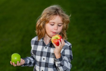 Téléchargez les photos : Apple child. Portrait of kid biting an apple. Child bites big apple, against green summer garden - en image libre de droit