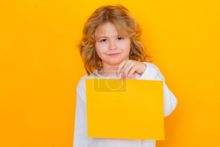 Foto de Happy child with sheet of paper, isolated on yellow background. Empty board for templates banner, copy spase, mock up. Happy kid, happy and smiling emotions - Imagen libre de derechos