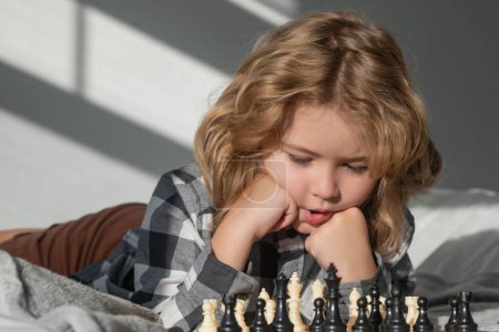 Téléchargez les photos : Clever child thinking about chess. Portrait of clever kid with chessboard. Boy play chess. Children playing chess at home - en image libre de droit