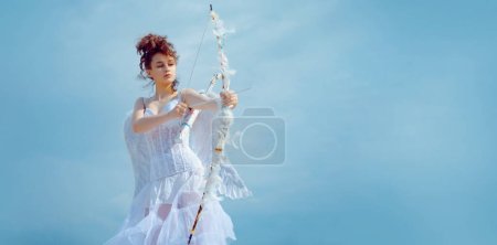 Téléchargez les photos : Banner. Angel teenager girl with white wings. Teenager angel girl with wings aiming with bow and arrow, copy space on sky. Banner flyer template for advertising or for website header design - en image libre de droit