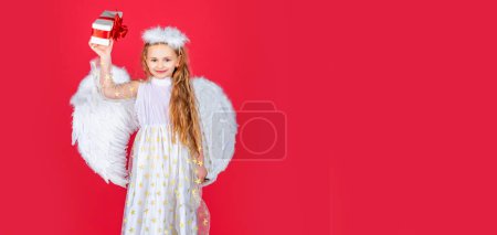 Téléchargez les photos : Angel child banner, isolated studio background. Child angel little girl with present gift, studio portrait. Little angel, happy fairy with white wings holds gift - en image libre de droit