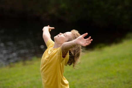 Foto de Peaceful kid with raised hands meditating, feeling calm positive and relaxed on nature background. Kids yoga practice. Harmony with nature - Imagen libre de derechos