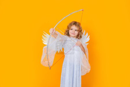 Téléchargez les photos : Angel child shoots a love arrow from a bow on Valentines Day. Little cupid angel child with wings. Studio portrait of angelic kid - en image libre de droit