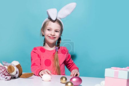 Téléchargez les photos : Mignon petit enfant portant des oreilles de lapin le jour de Pâques. Souriant fille tenant panier avec des œufs peints - en image libre de droit