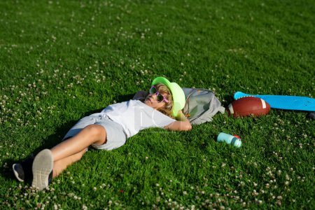Foto de Kid boy girl resting on green grass. Child relax at the summer park. Kid boy lying on green grass outdoor - Imagen libre de derechos