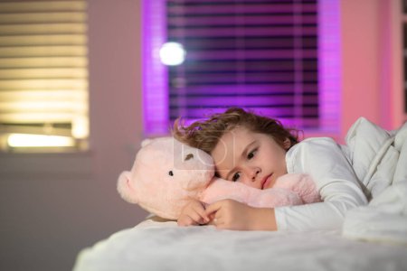 Téléchargez les photos : Child cannot sleep on bed at night in bedroom. Kid having sleeplessness. Kid boy sleeping in bed with night light - en image libre de droit